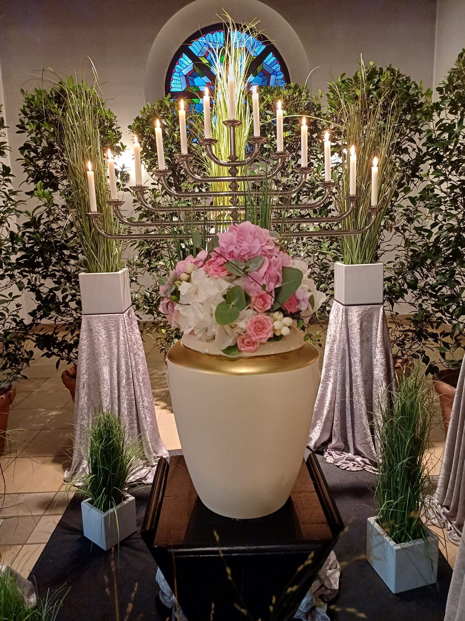 Eleganter Blumenaltar mit rosa Blumen, weißen Kerzen und hohem Grün in einem kirchenähnlichen Ambiente