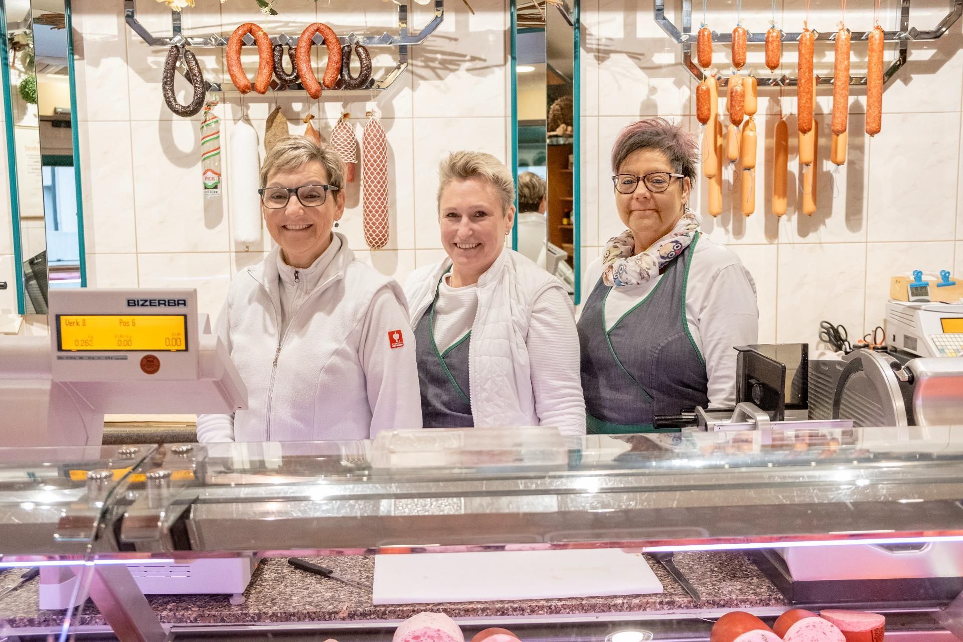 Metzgerei-Team bei der Arbeit an der Fleischtheke mit frischen Wurst- und Fleischwaren.