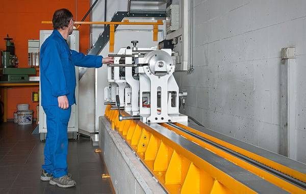 Eine Person in blauer Arbeitskleidung bedient Maschinen in einer Werkstatt. Gelbes Maschinenbett. Orangefarbene Wand.