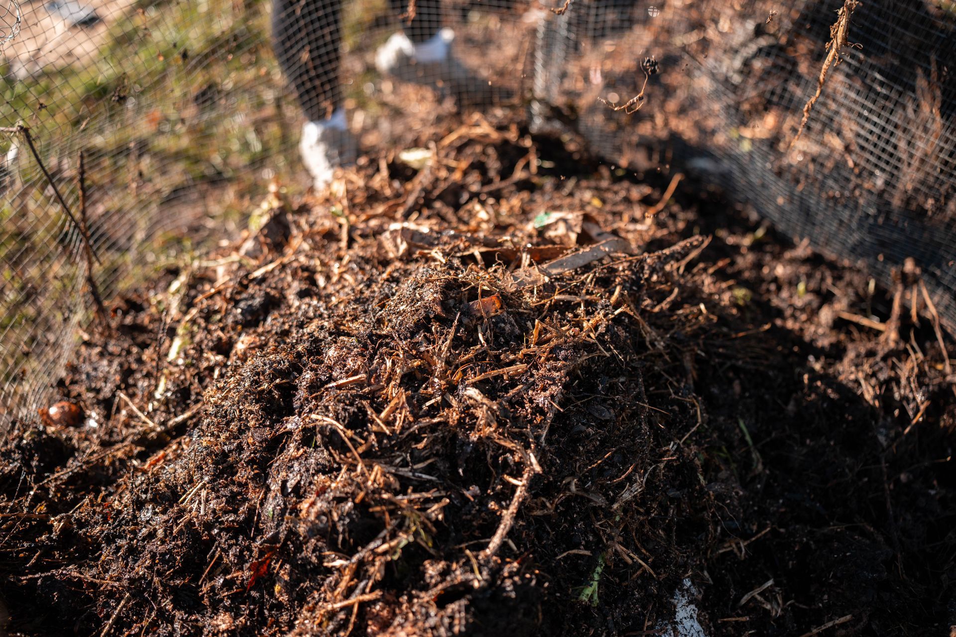 Tas de compost avec terre brun foncé et diverses matières organiques sous un filet à mailles.