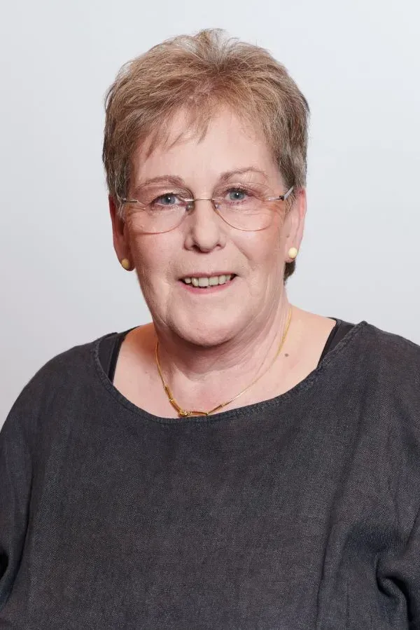 Eine Frau mit Brille und Ohrringen lächelt in die Kamera.