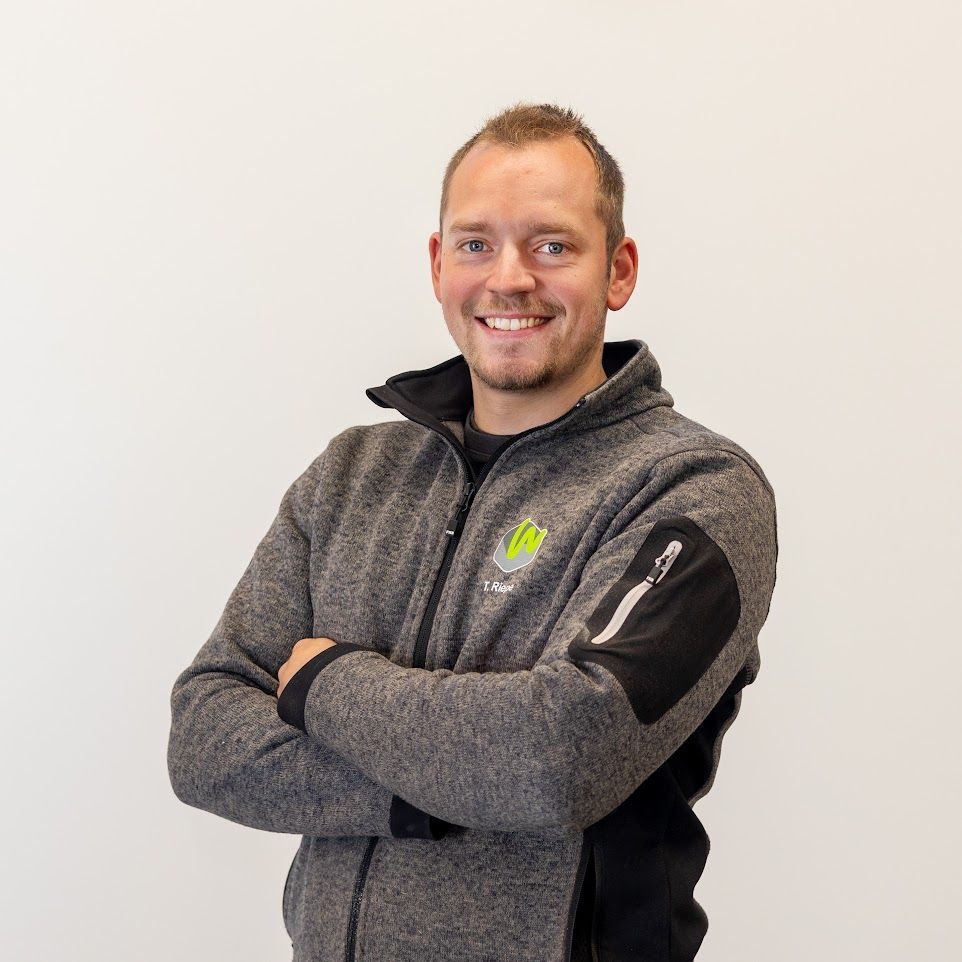 Ein Mann mit verschränkten Armen trägt ein graues Sweatshirt