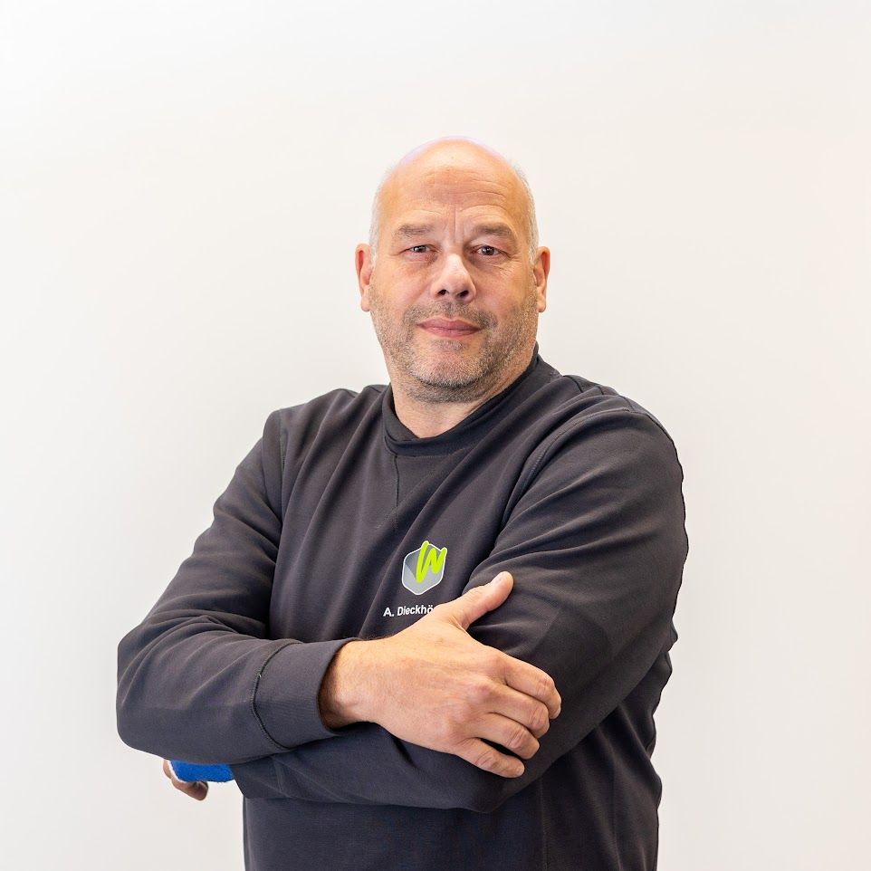 Ein kahlköpfiger Mann, der einen grauen Pullover mit einem grünen Blatt darauf trägt