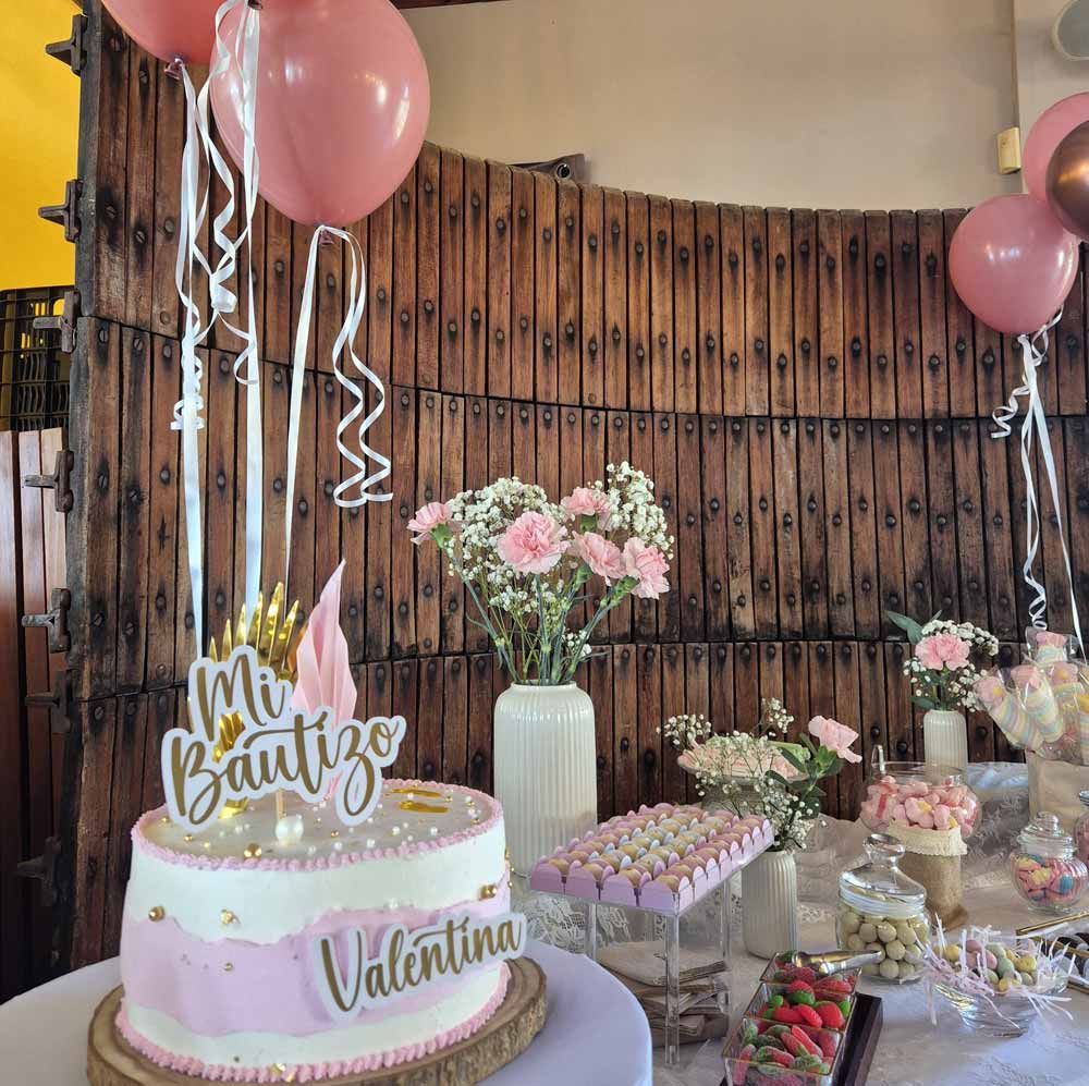Mesa de pastel y dulces para el bautizo de Valentina. Decoración rosa y blanca con globos y flores.