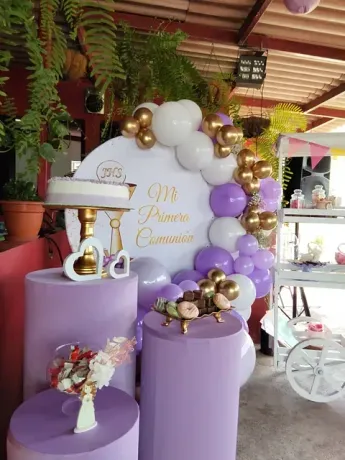 Una habitación decorada con globos morados, blancos y dorados y un soporte para pasteles.