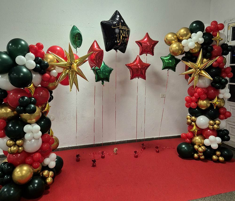Arco de globos en rojo, negro, dorado y blanco, con globos de estrellas contra una pared blanca y alfombra roja.