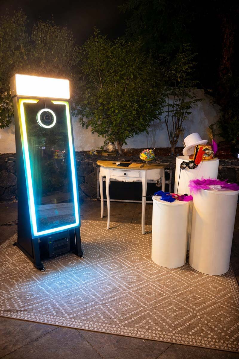 Fotomatón con luces de colores al aire libre; accesorios en mesas cercanas.