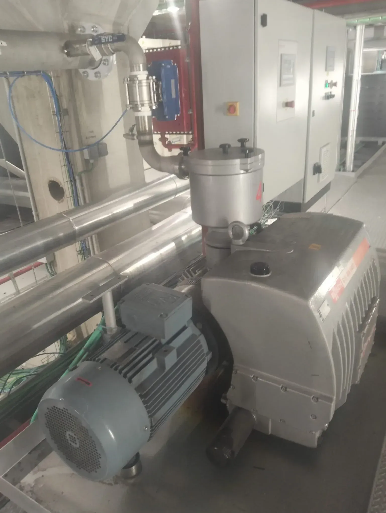 Bomba de vacío industrial conectada a tuberías metálicas en una sala de máquinas.