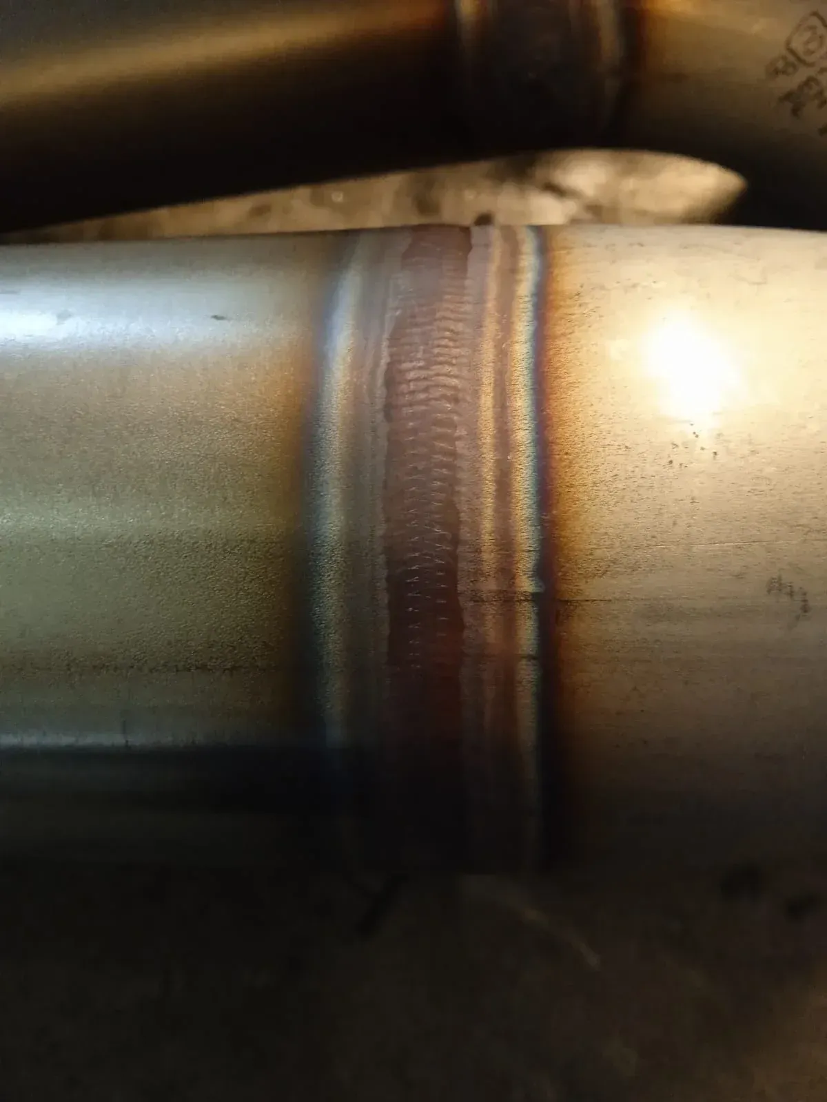 Primer plano de dos tubos metálicos unidos por una soldadura con decoloración por calor.