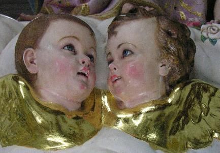 Duas estátuas angelicais com asas douradas, olhando para cima com bochechas rosadas.