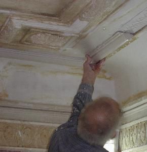Homem trabalhando em moldura decorativa de teto; foto interna.