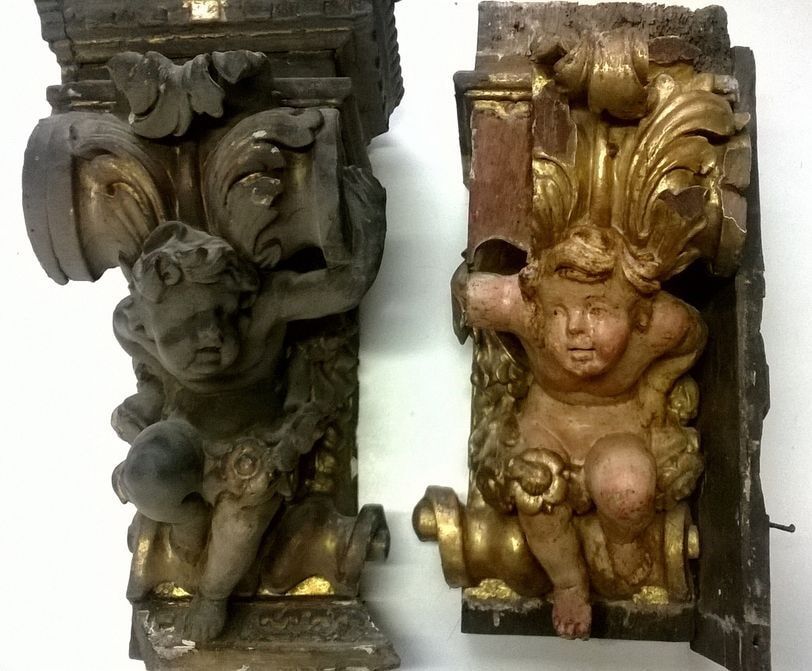 Dois suportes de prateleira antigos de madeira em forma de querubim; um escuro e outro dourado.
