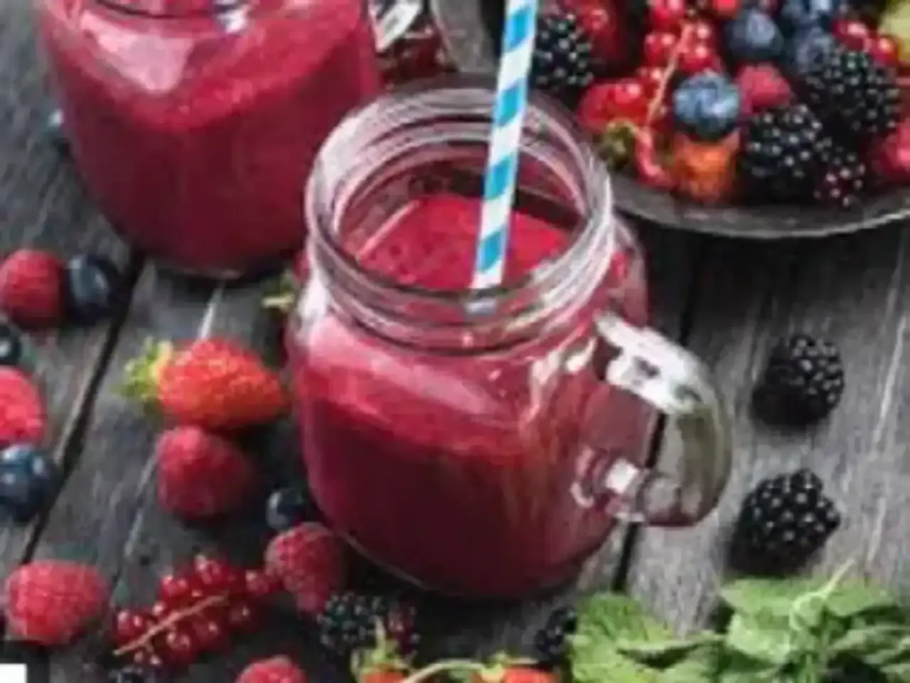 Batido de bayas en frasco de vidrio con fruta sobre una mesa de madera.