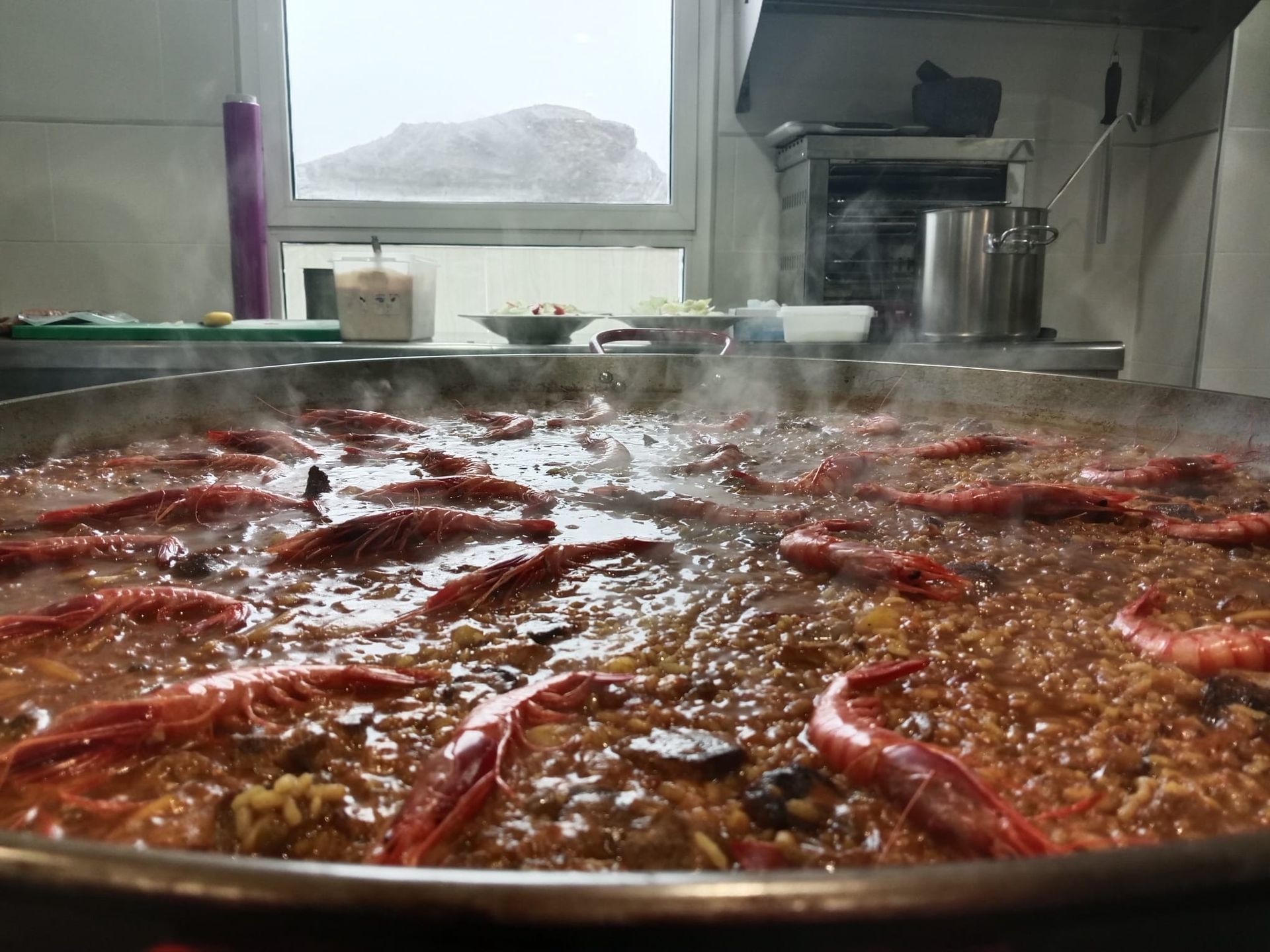 En una cocina se está cocinando una sartén grande llena de camarones y arroz.