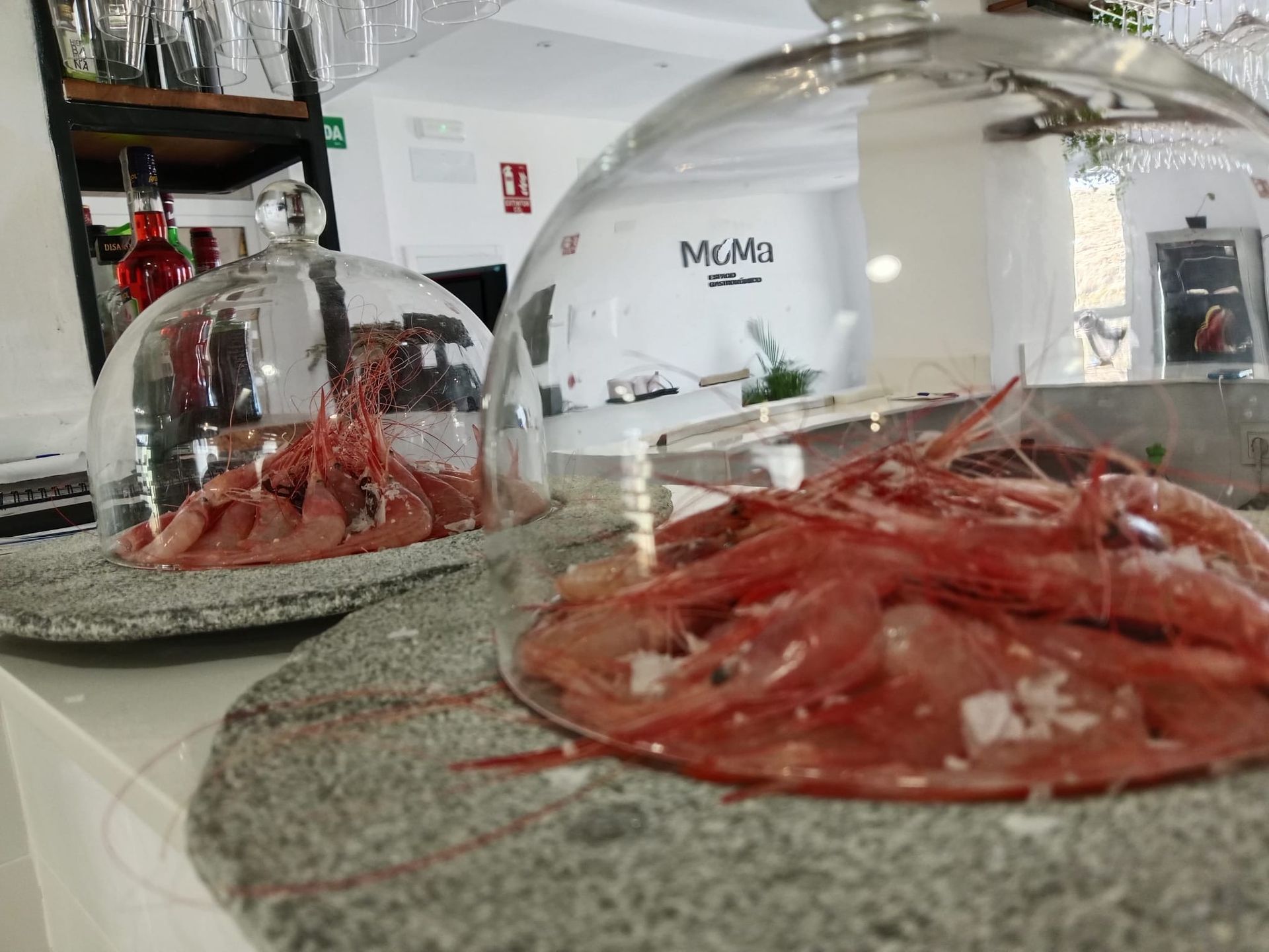 Dos platos de camarones bajo una cúpula de cristal sobre una mesa.