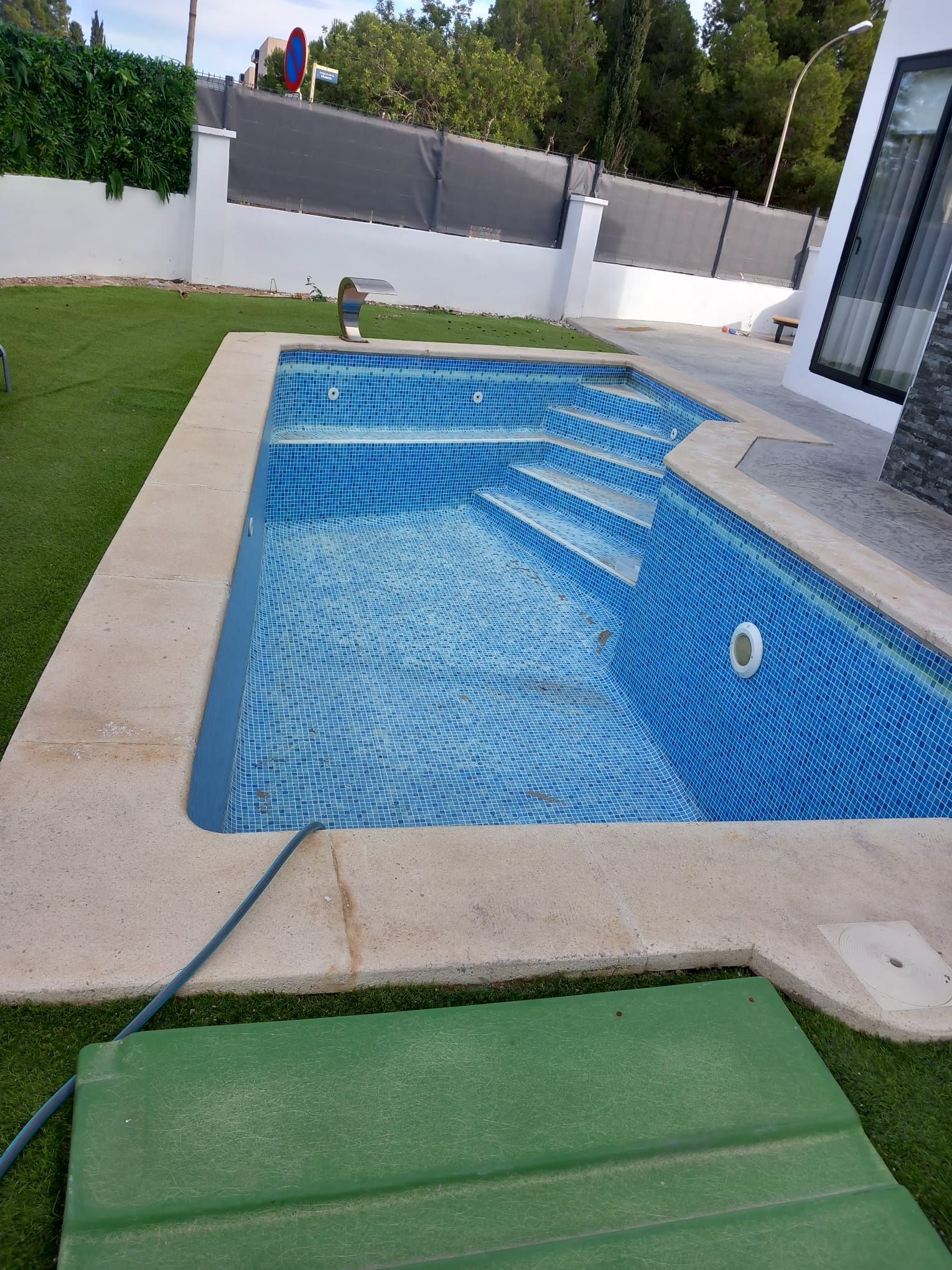 Una gran piscina está rodeada de césped y una valla.