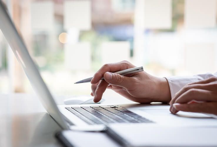 Hände tippen mit einem Stift auf einem Laptop in einer hellen Büroumgebung