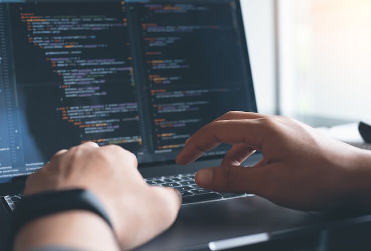 Hände tippen auf einem Laptop mit Code auf dem Bildschirm in einem schwach beleuchteten Arbeitsbereich