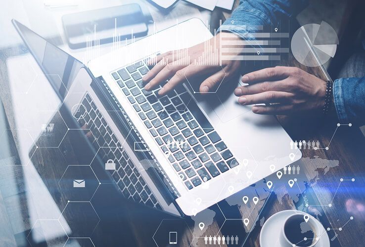 Hände, die auf einem Laptop mit überlagerten digitalen Benutzeroberflächensymbolen auf einem blauen Schreibtisch tippen