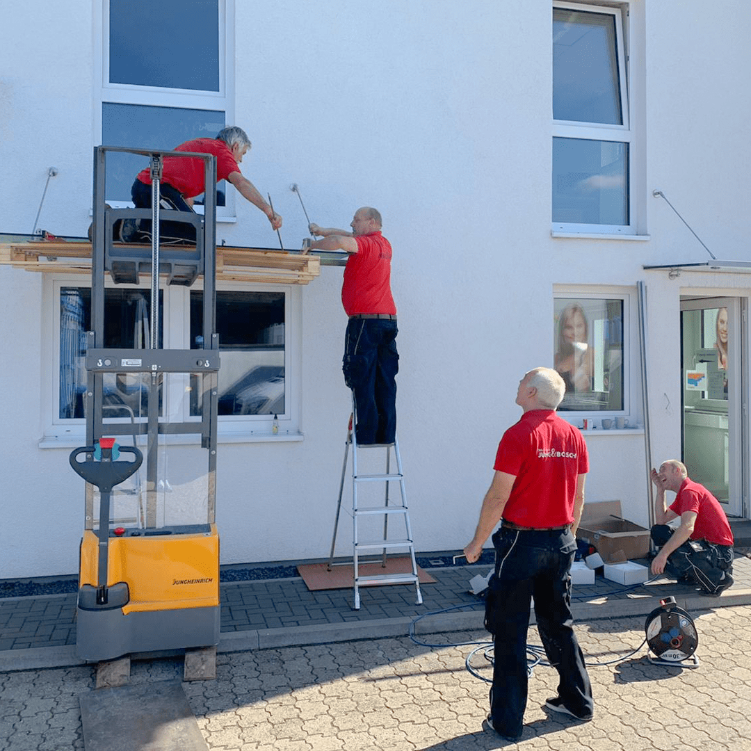 Drei Männer in roten Hemden arbeiten an einem Gebäude