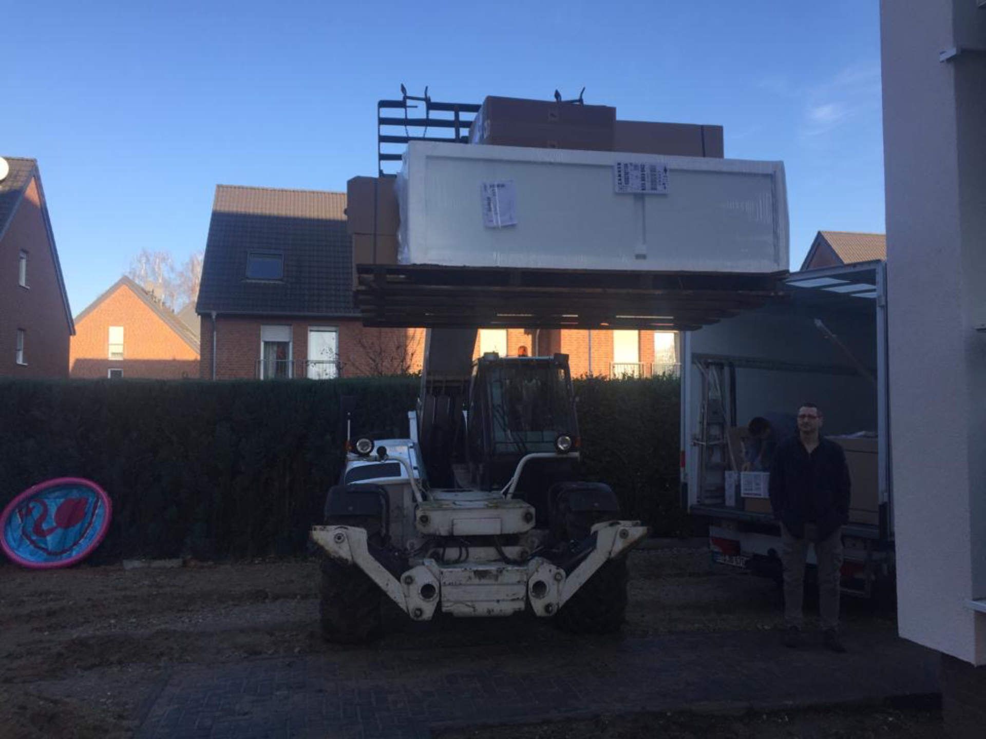 Ein Gabelstapler hebt eine große weiße Kiste auf ein Gebäude