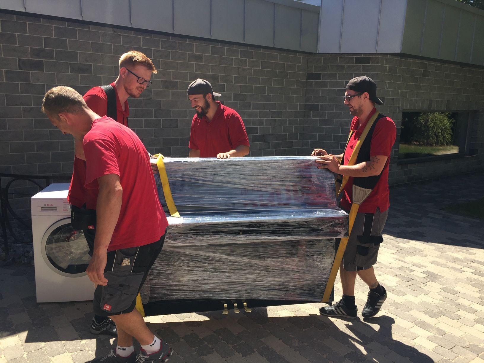 Eine Gruppe Männer trägt ein in Plastik eingewickeltes Sofa.