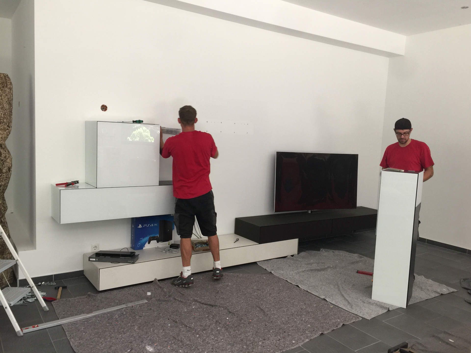 Zwei Männer stehen in einem Wohnzimmer und halten Holzstücke.