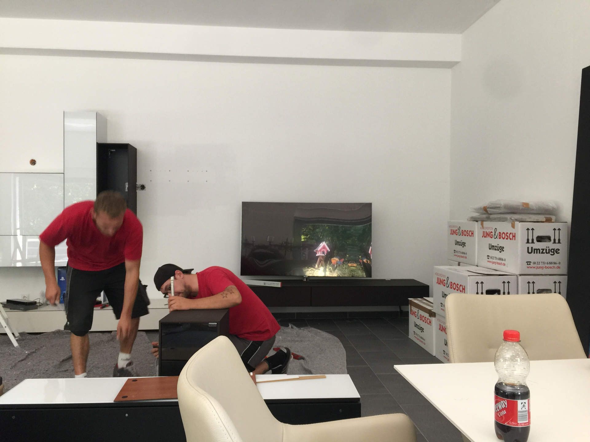 Zwei Männer arbeiten an einem Tisch in einem Wohnzimmer.