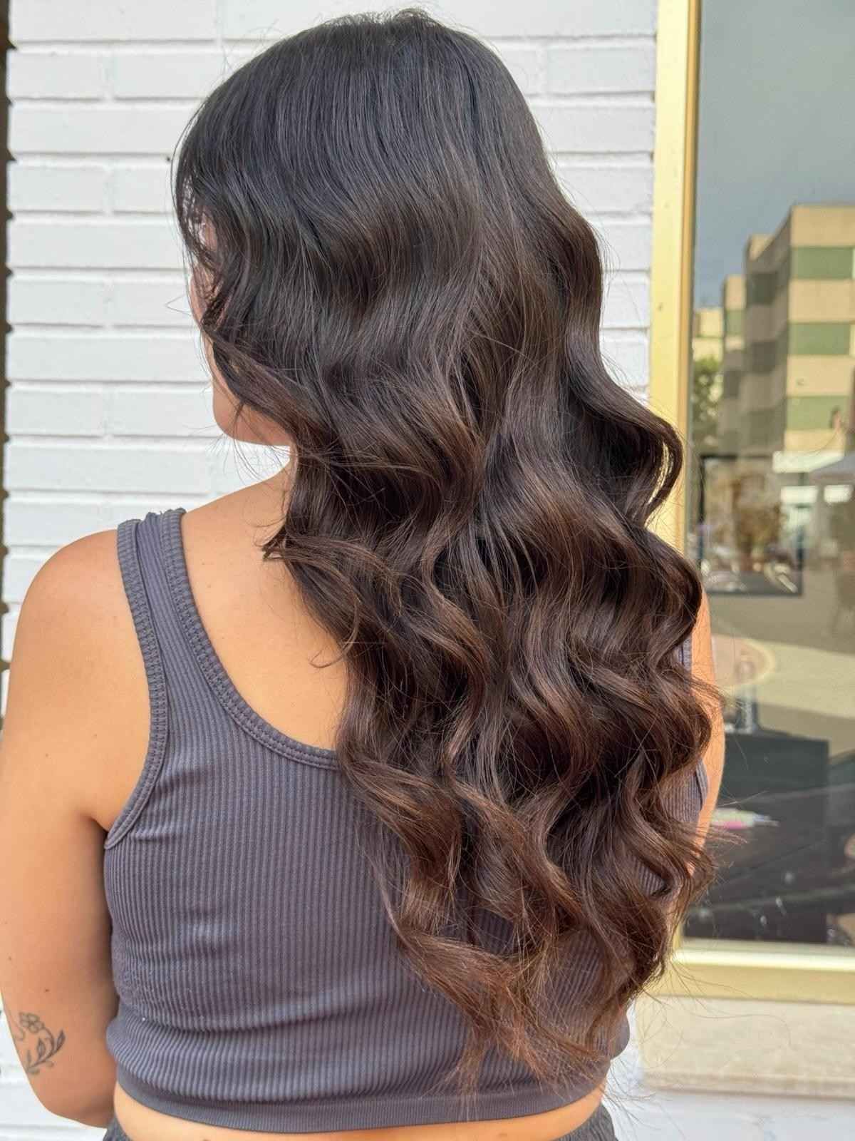 Mujer con cabello oscuro y ondulado, vestida con una camiseta sin mangas de canalé gris, posando al aire libre cerca de un edificio.