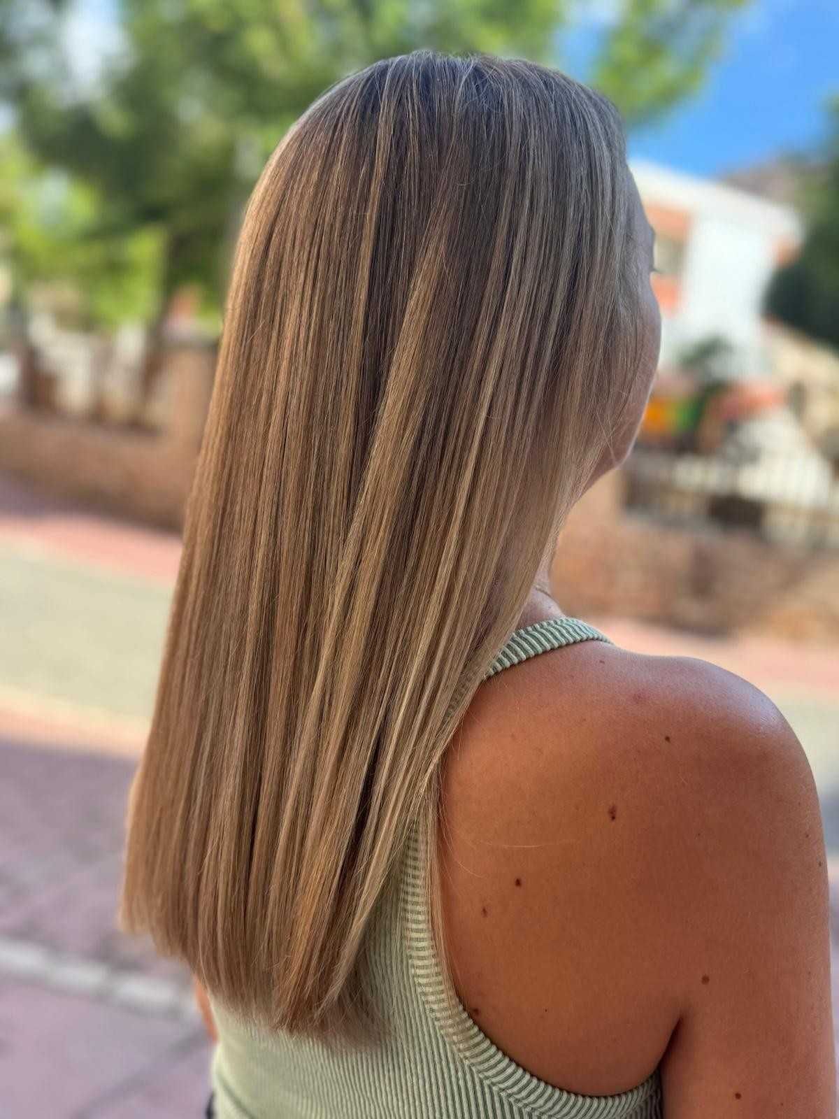 Mujer con cabello largo, liso y castaño claro, vestida con una camiseta sin mangas verde, al aire libre.