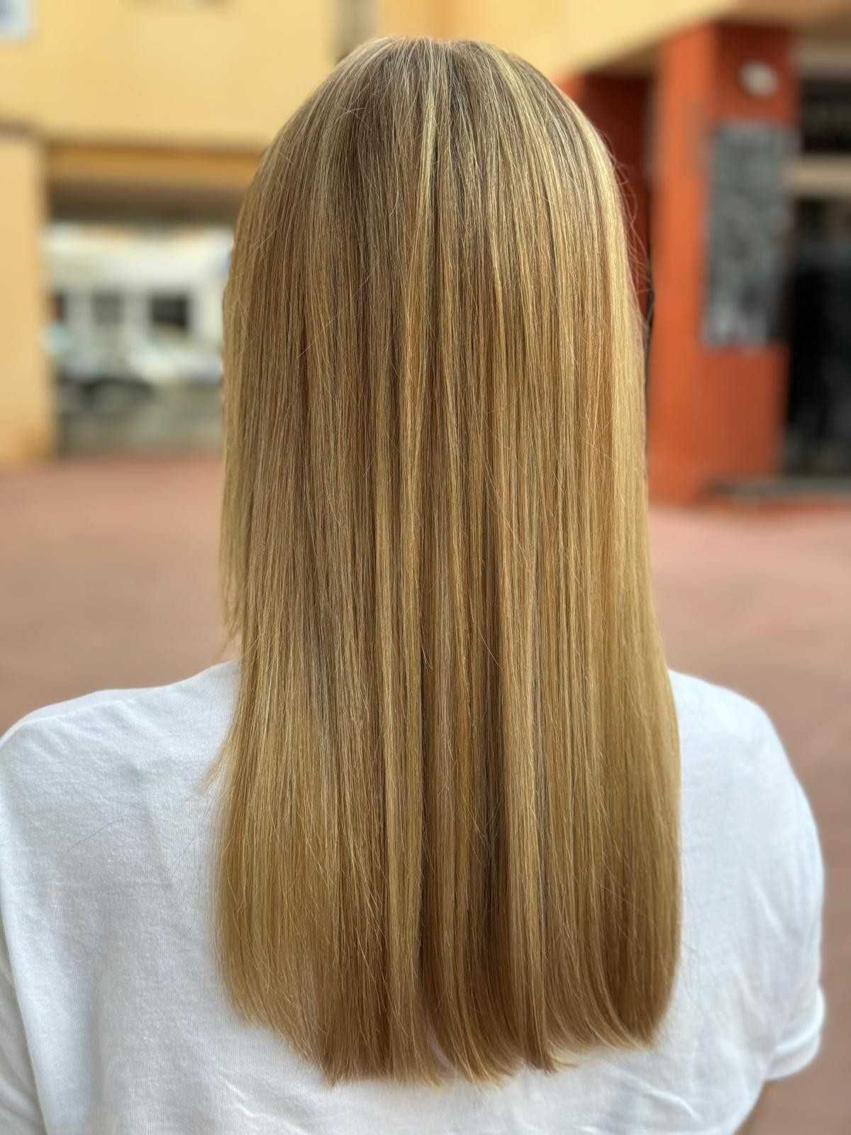 Mujer con cabello largo, liso y rubio, vista desde atrás, vistiendo una camisa blanca, al aire libre.