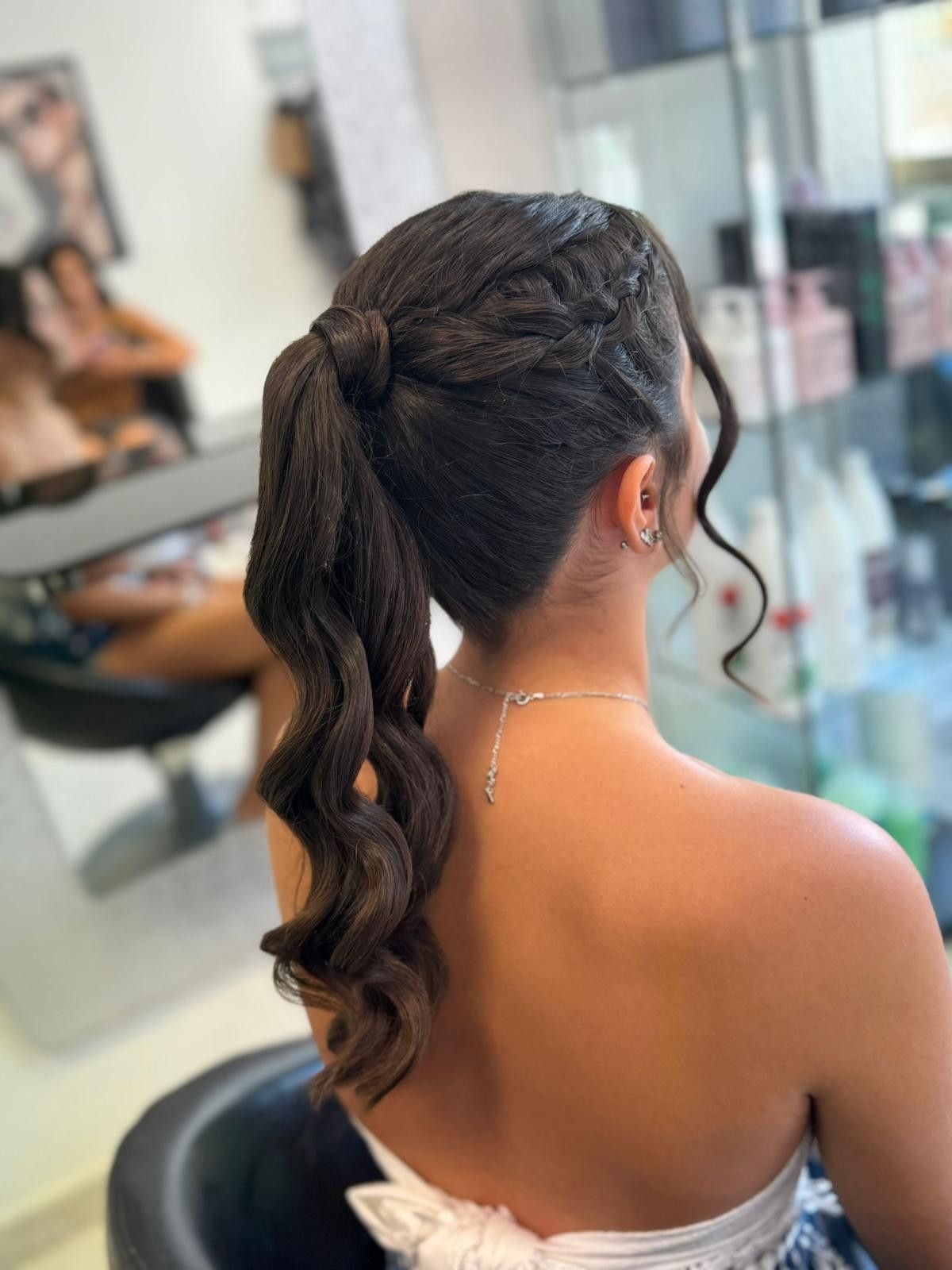 Mujer con cabello oscuro recogido en una cola trenzada con grandes rizos, vistiendo un top sin tirantes.