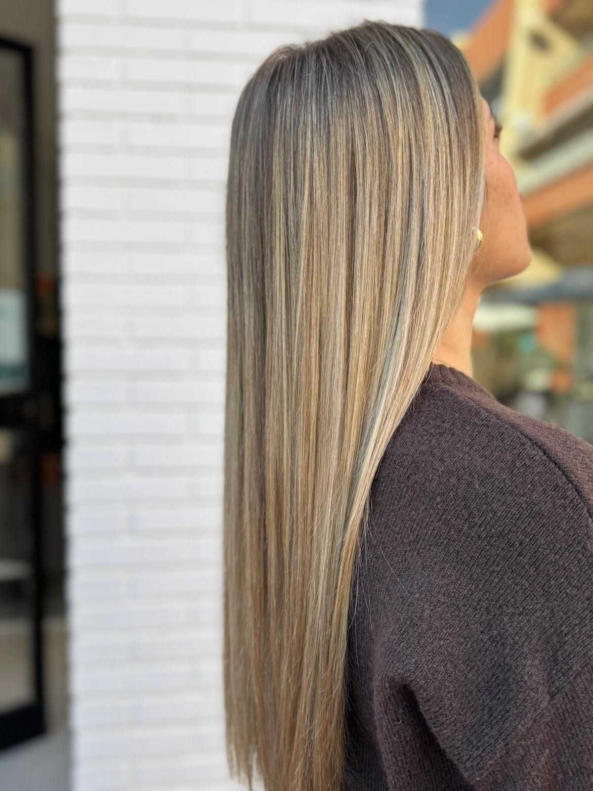 Mujer con cabello rubio largo, liso y con reflejos, al aire libre, con top marrón.