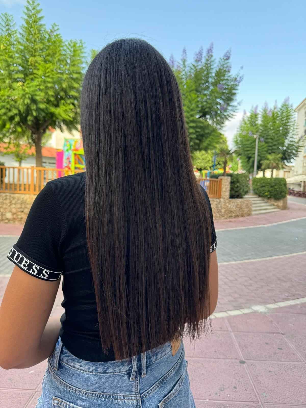Mujer con cabello largo, liso y oscuro, vestida con una camisa negra y jeans en un parque.