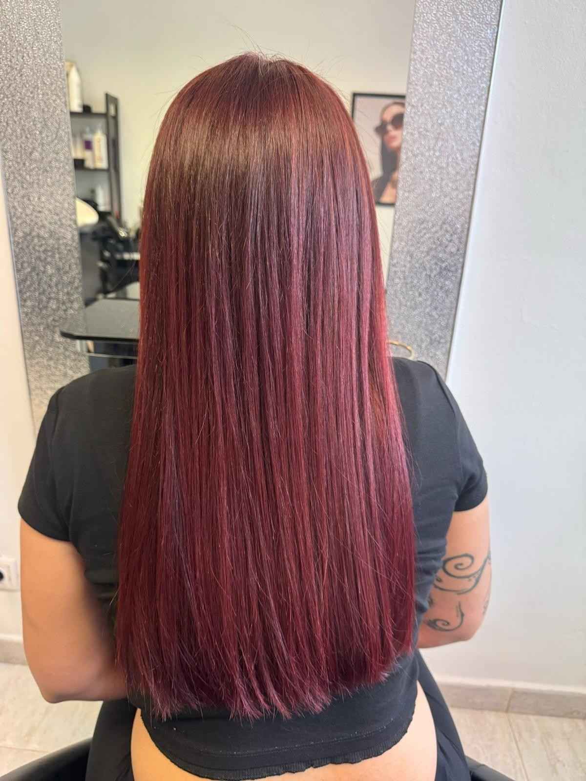 Mujer con cabello lacio y de color rojo intenso en una silla de salón.