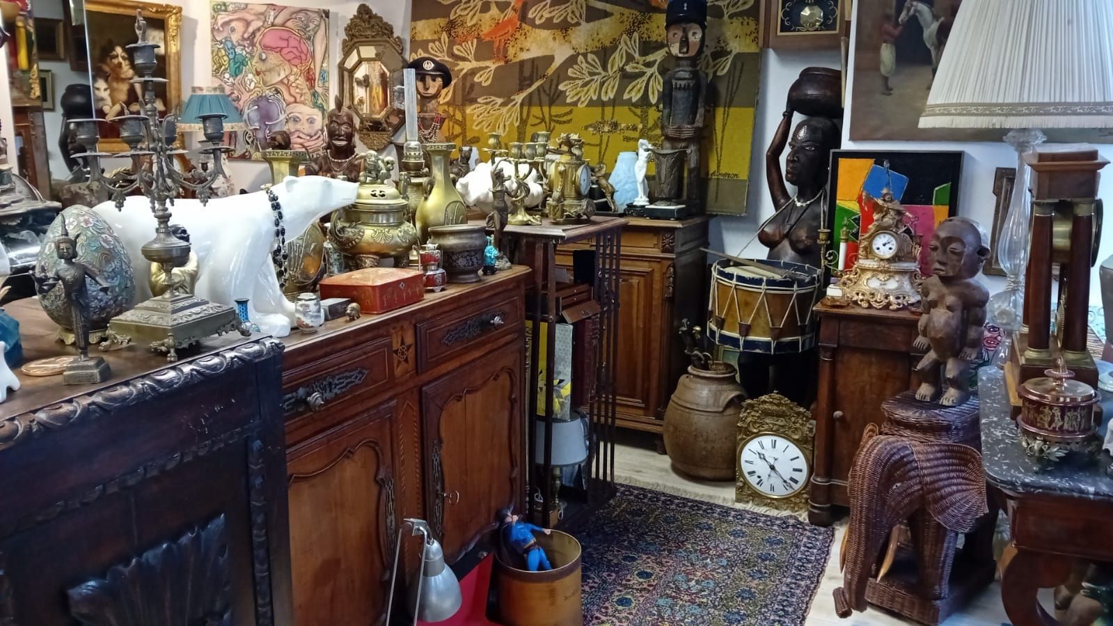 Intérieur d'un magasin d'antiquités, rempli de meubles, de sculptures, de lampes, d'horloges et d'objets décoratifs.