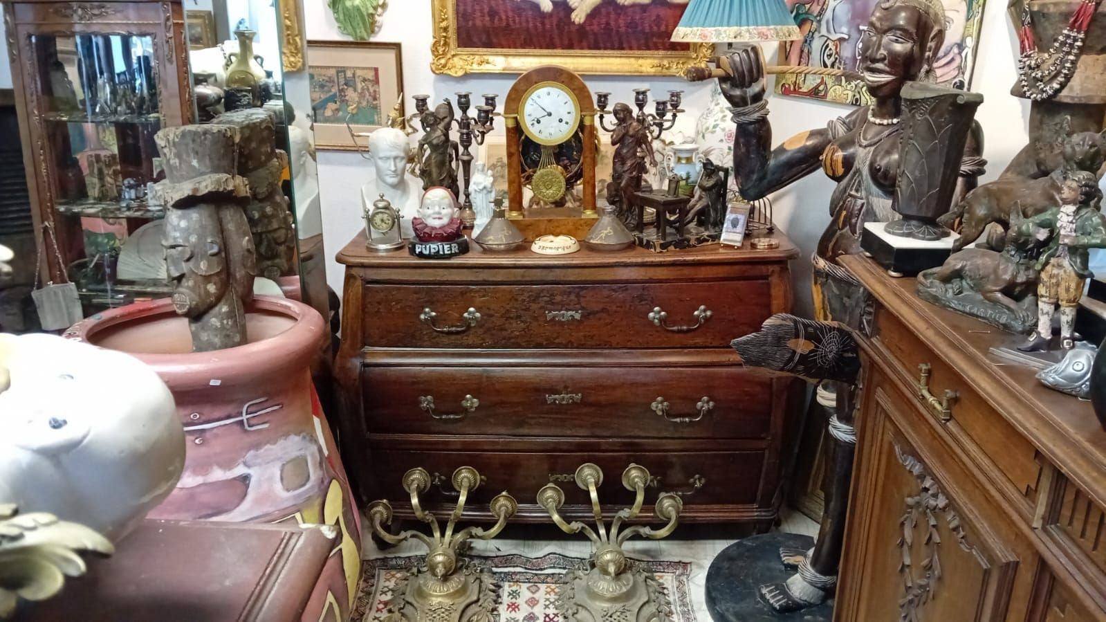 Commode ancienne en bois ornée de divers objets décoratifs, exposée dans une boutique d'antiquités encombrée.
