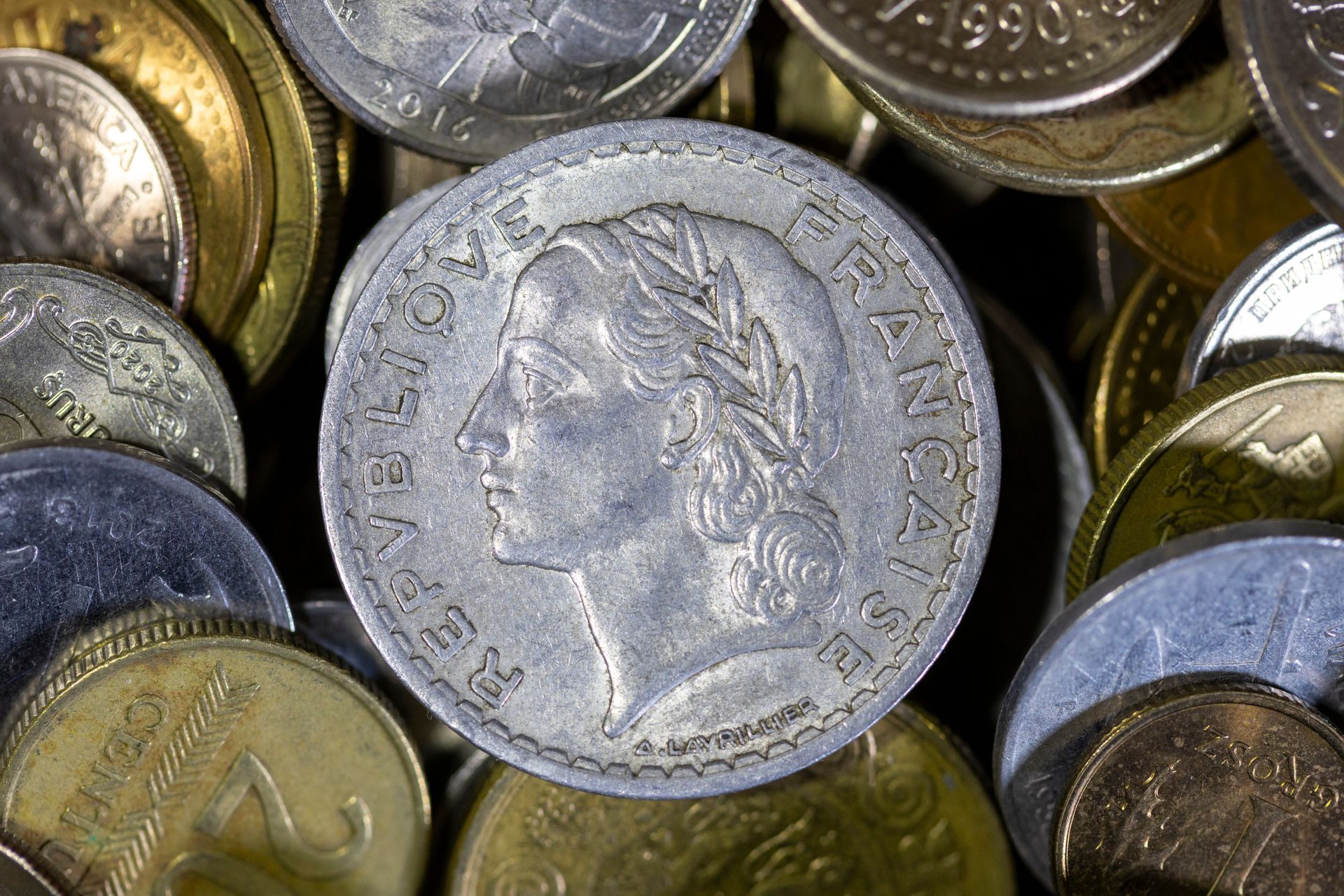 Pile de pièces de monnaie, avec une pièce française en argent représentant le profil d'une femme au centre.