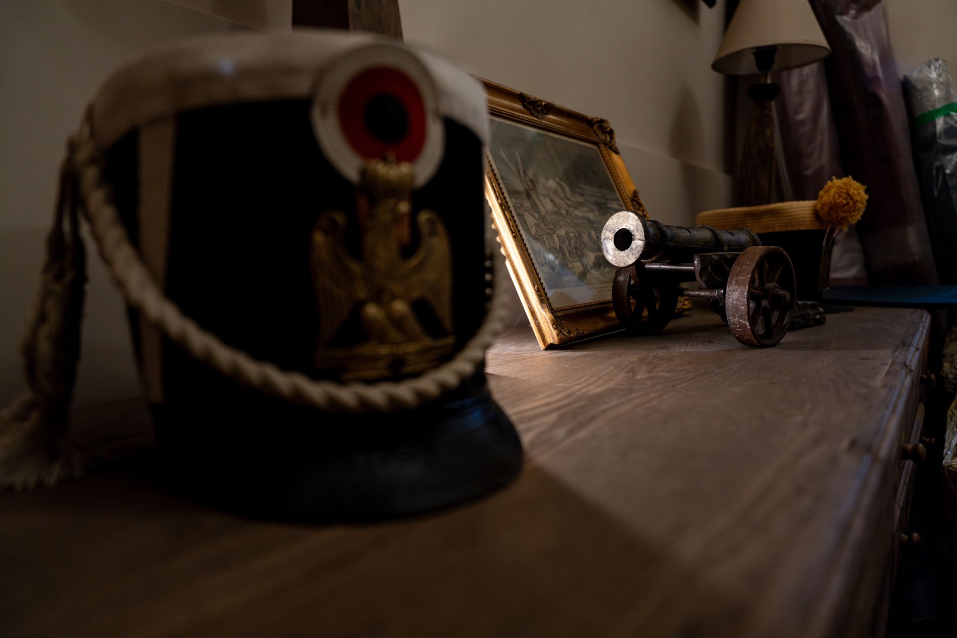 Un chapeau noir orné d'un emblème doré et un canon miniature sur une surface en bois.