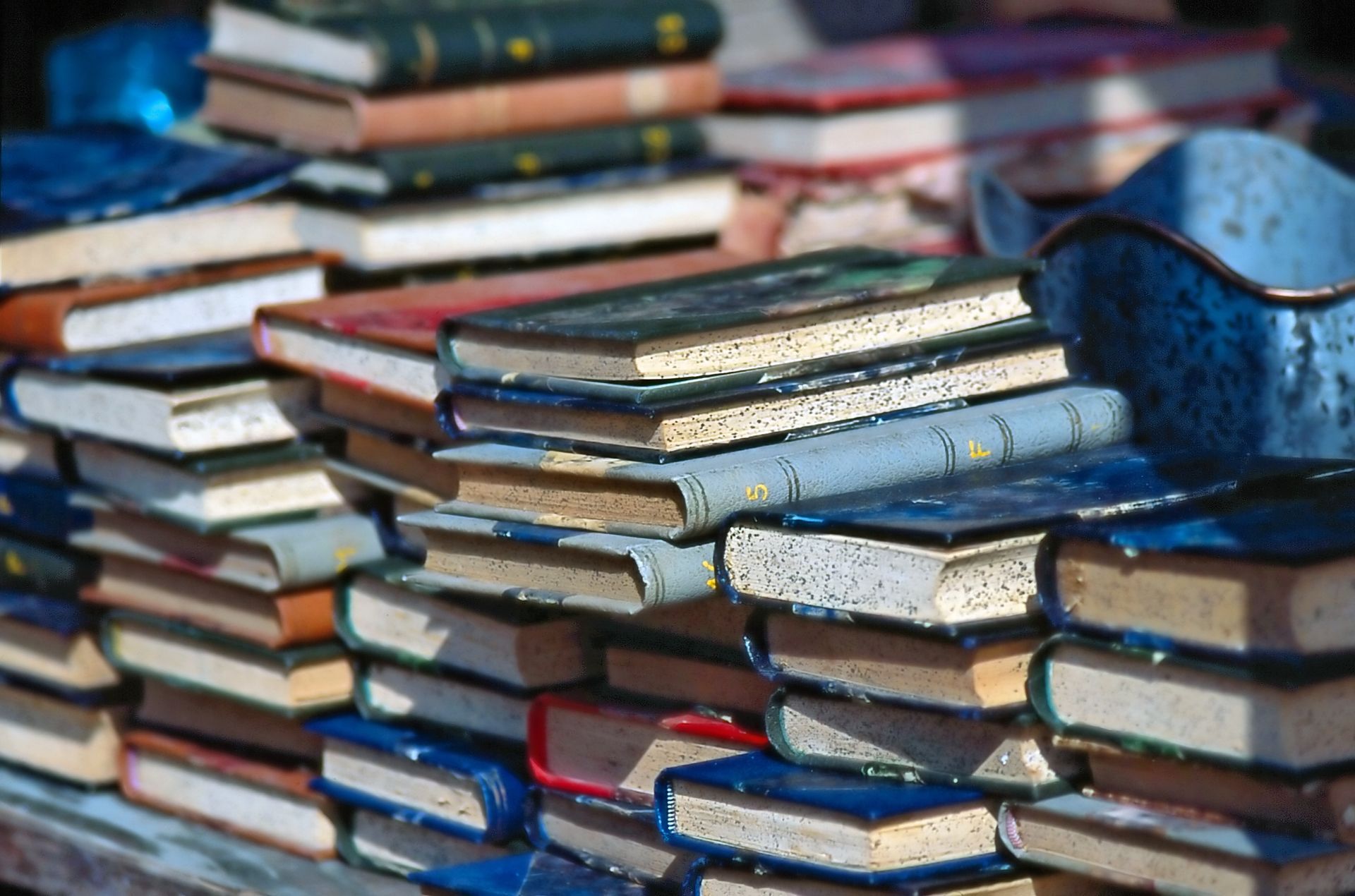 Des piles de vieux livres colorés sur une table, avec des dos bleus, rouges, verts et bruns.
