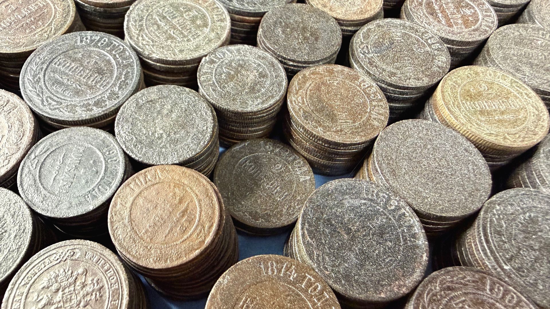 Des piles de pièces de monnaie anciennes, rondes et patinées par le temps, certaines portant des marques visibles.