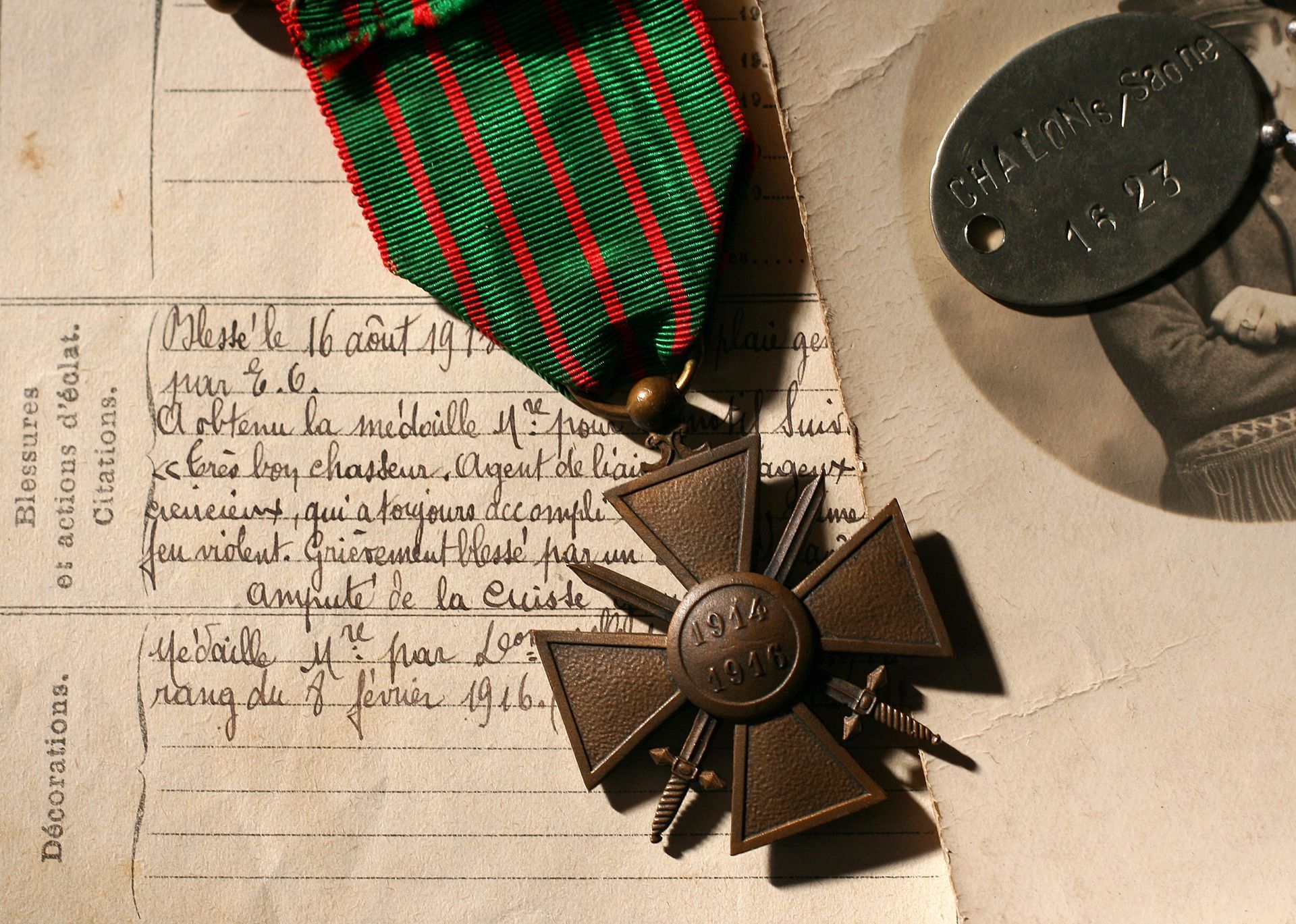 Médaille avec ruban, plaque d'identité et document. Médaille croix brune sur ruban rayé vert et rouge, à côté de la plaque d'identité et d'une photographie.