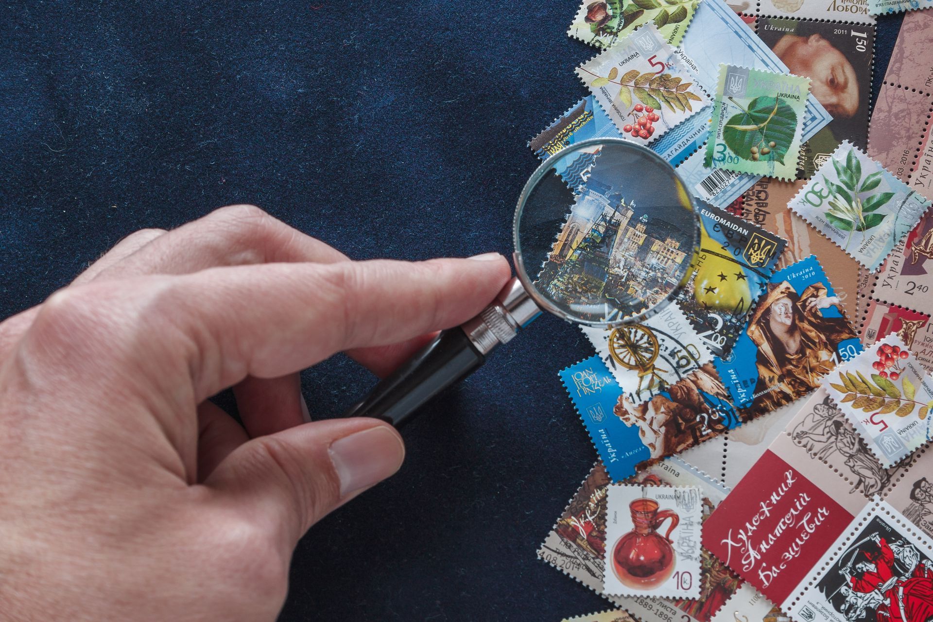 Une main tenant une loupe au-dessus d'une collection de timbres colorés sur une surface sombre.