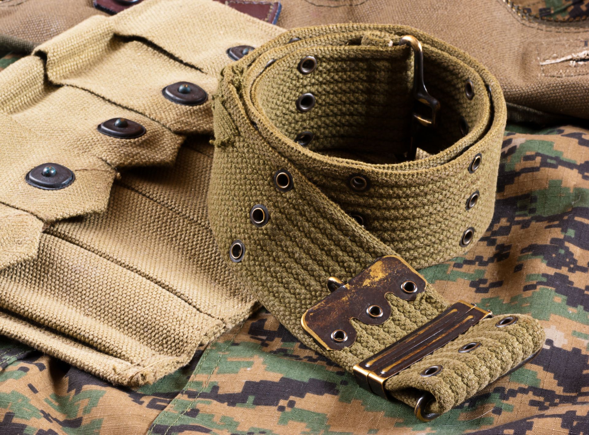 Ceinture militaire en toile verte avec boucle en laiton, posée sur un motif camouflage.