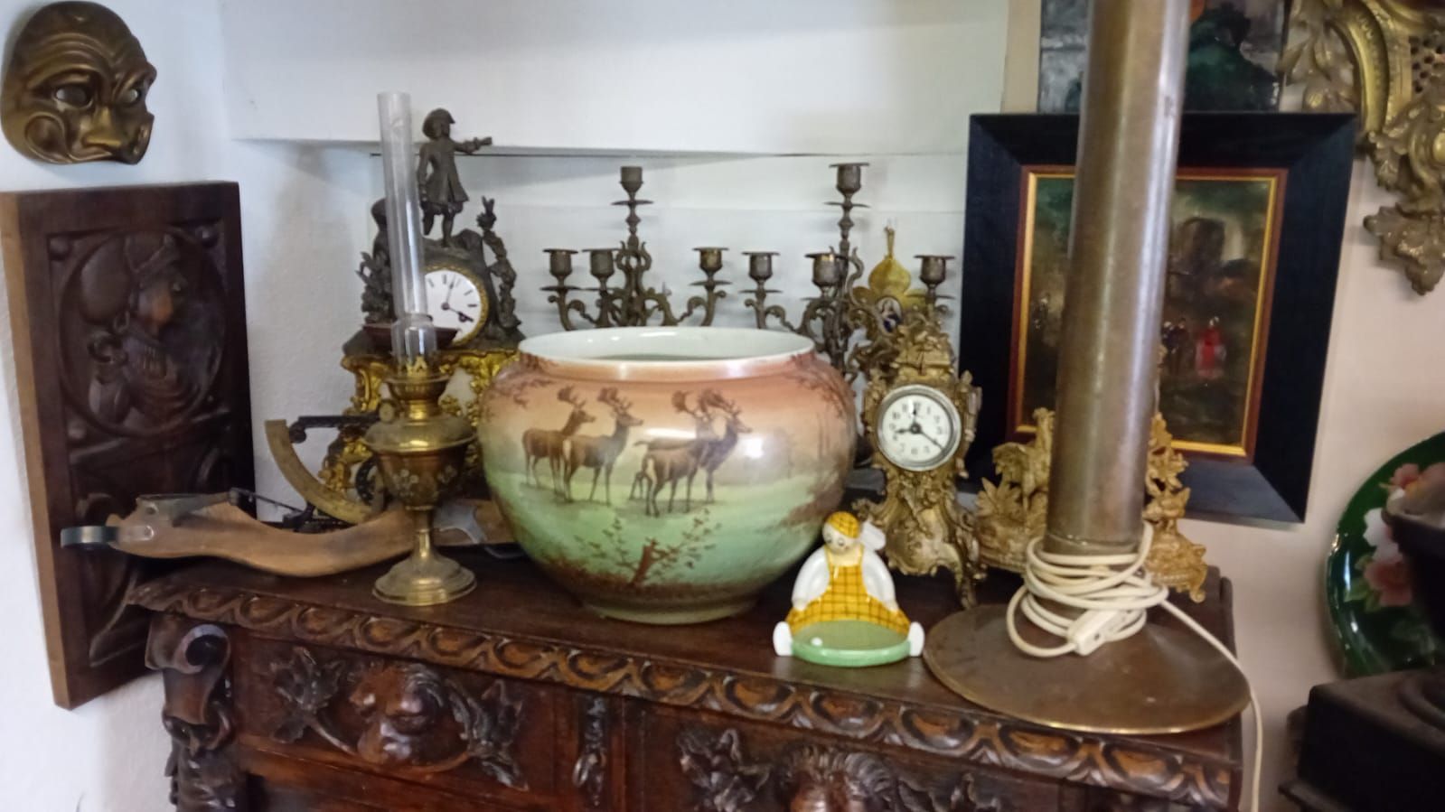 Un meuble ancien en bois expose des horloges ornées, des chandeliers et un vase à motif de cerf.