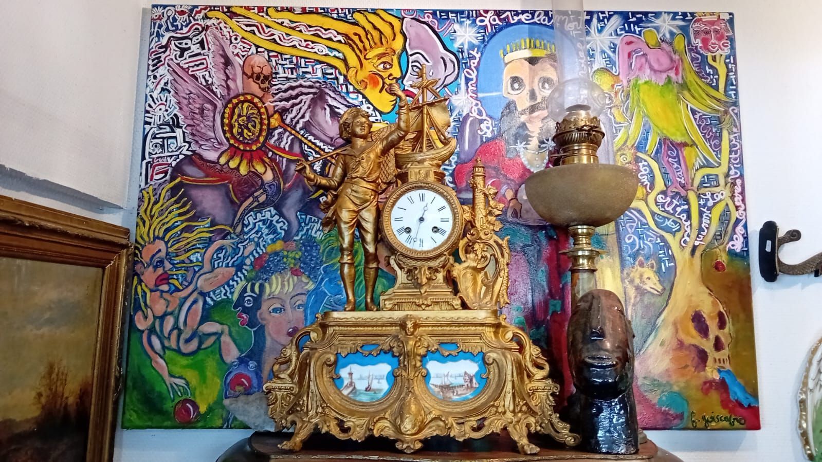 Une horloge dorée ornée repose sur une étagère, devant un tableau abstrait coloré.