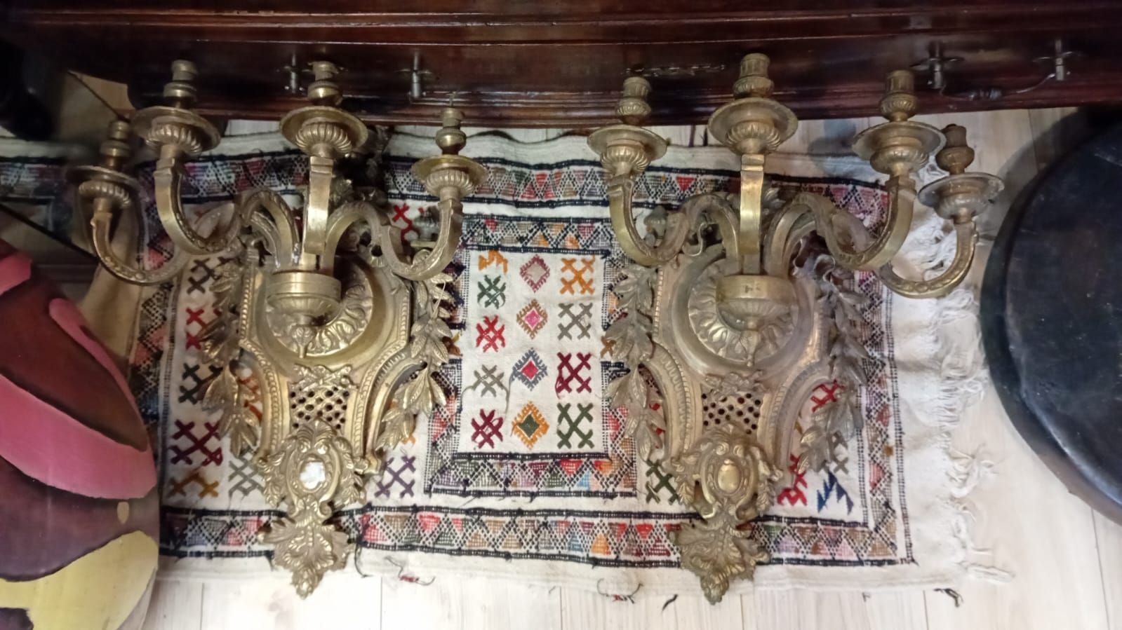 Deux appliques murales ornementées de couleur dorée, à plusieurs bras, sur un tapis à motifs.