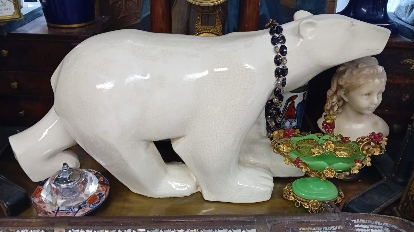Statue d'ours polaire en céramique blanche portant un collier, à côté d'un buste et d'un bijou orné de pierres précieuses.