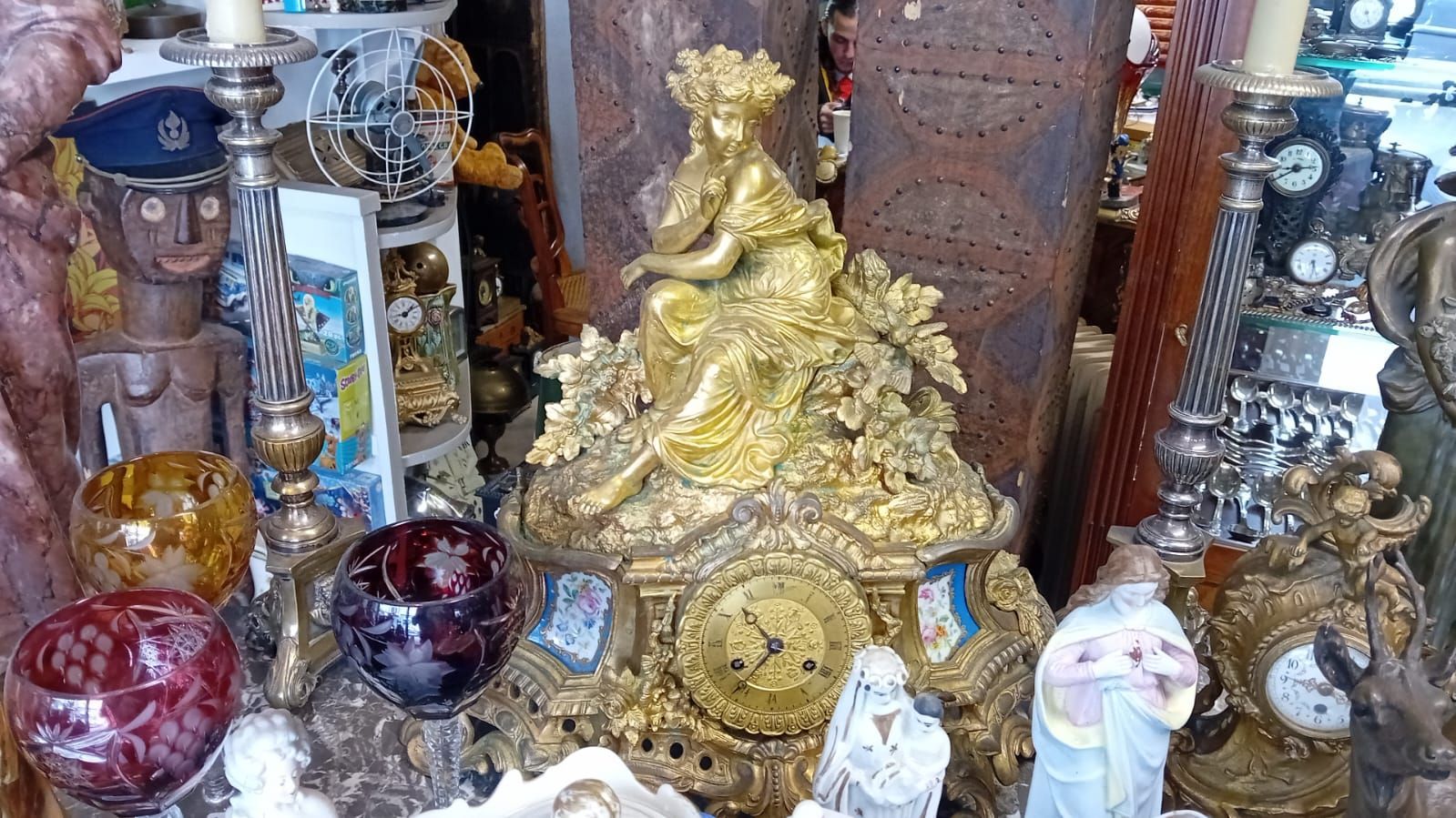 Vitrine d'antiquités, une horloge dorée ornée en pièce maîtresse, entourée de divers objets décoratifs.