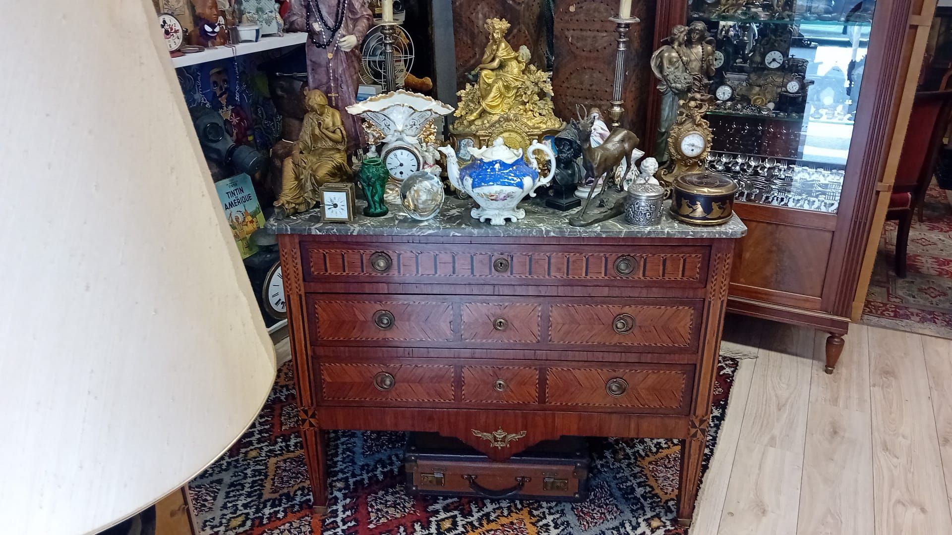 Commode ancienne en bois avec plateau en marbre, ornée de figurines et d'horloges, dans une boutique.